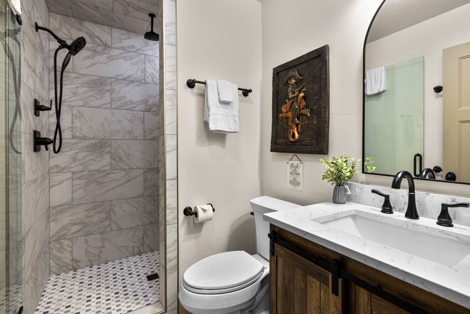 Modern bathroom with walk-in shower, white vanity, and toilet besides marble-look tile and black fixtures