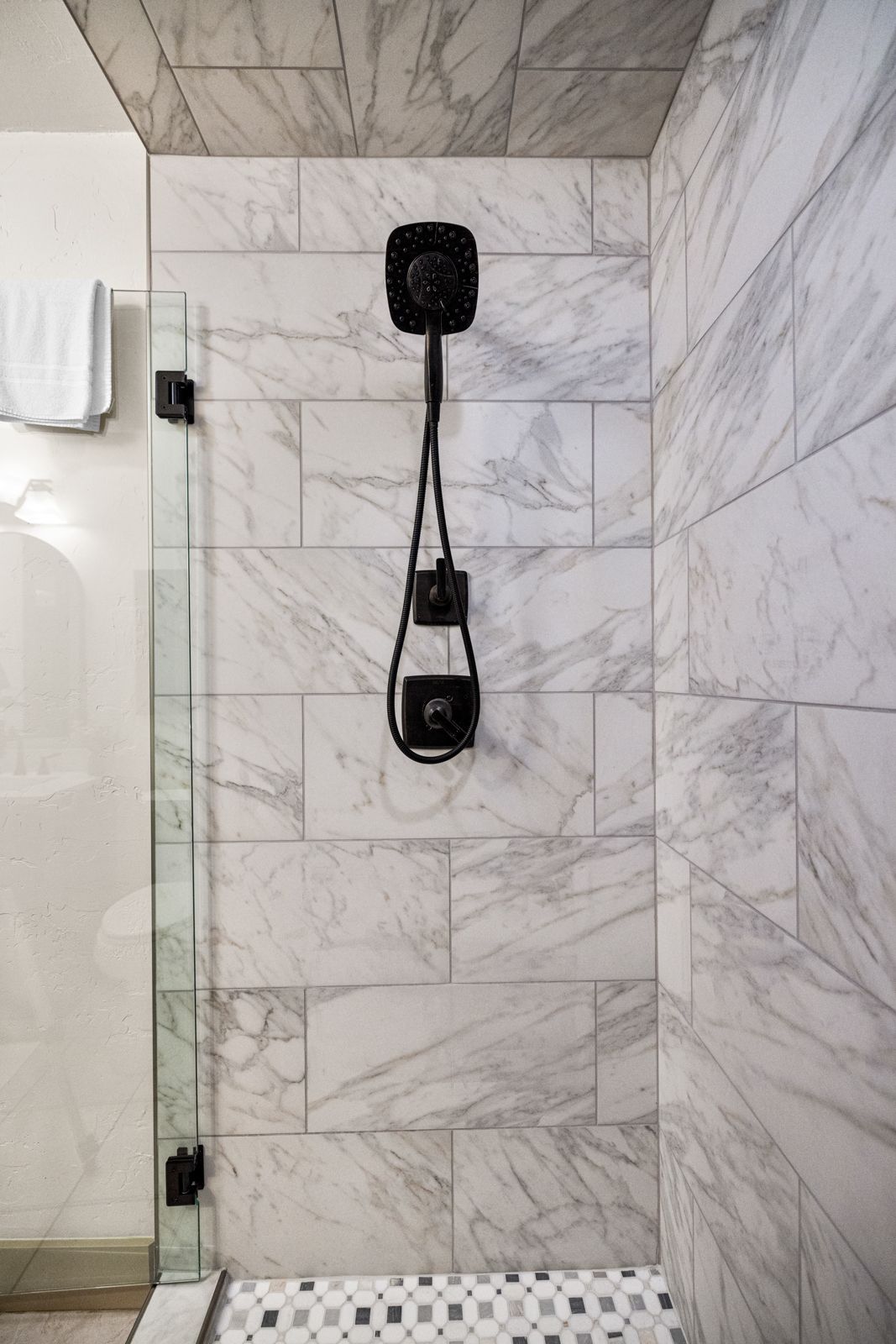 Shower stall with marble-pattern tile and a black showerhead and control fixture on the wall