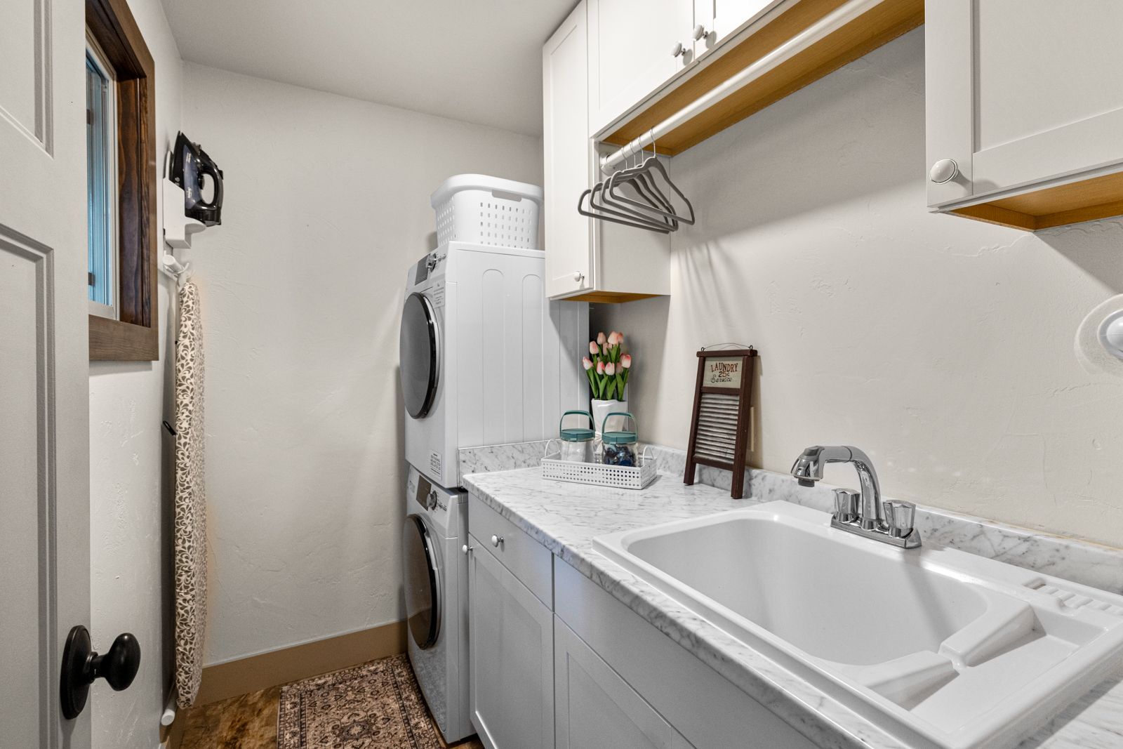 Narrow laundry room with stacked washer-dryer, utility sink, and wall-mounted shelves with cleaning supplies