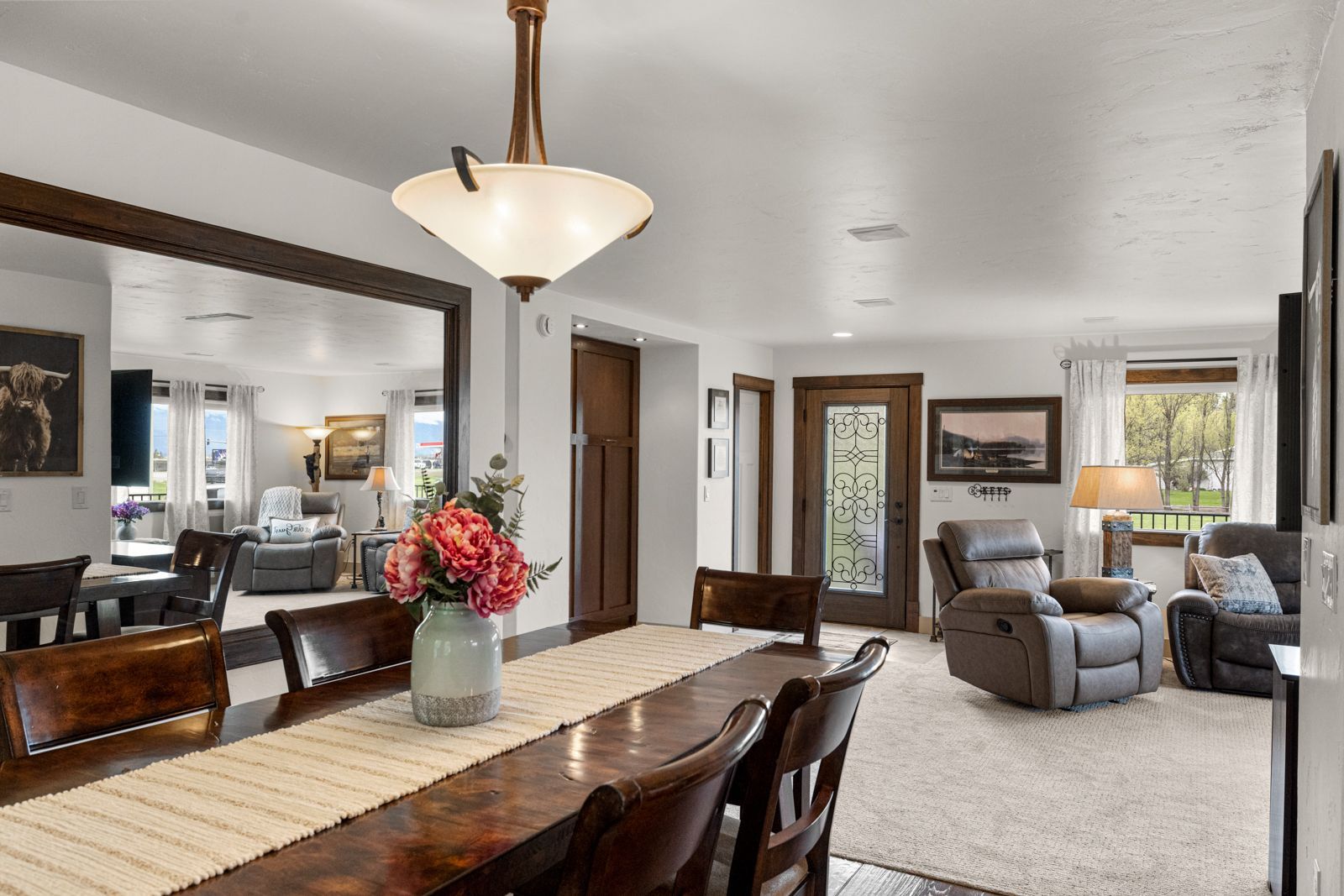 Open-concept dining and living room with wood furniture, gray recliner, and large windows
