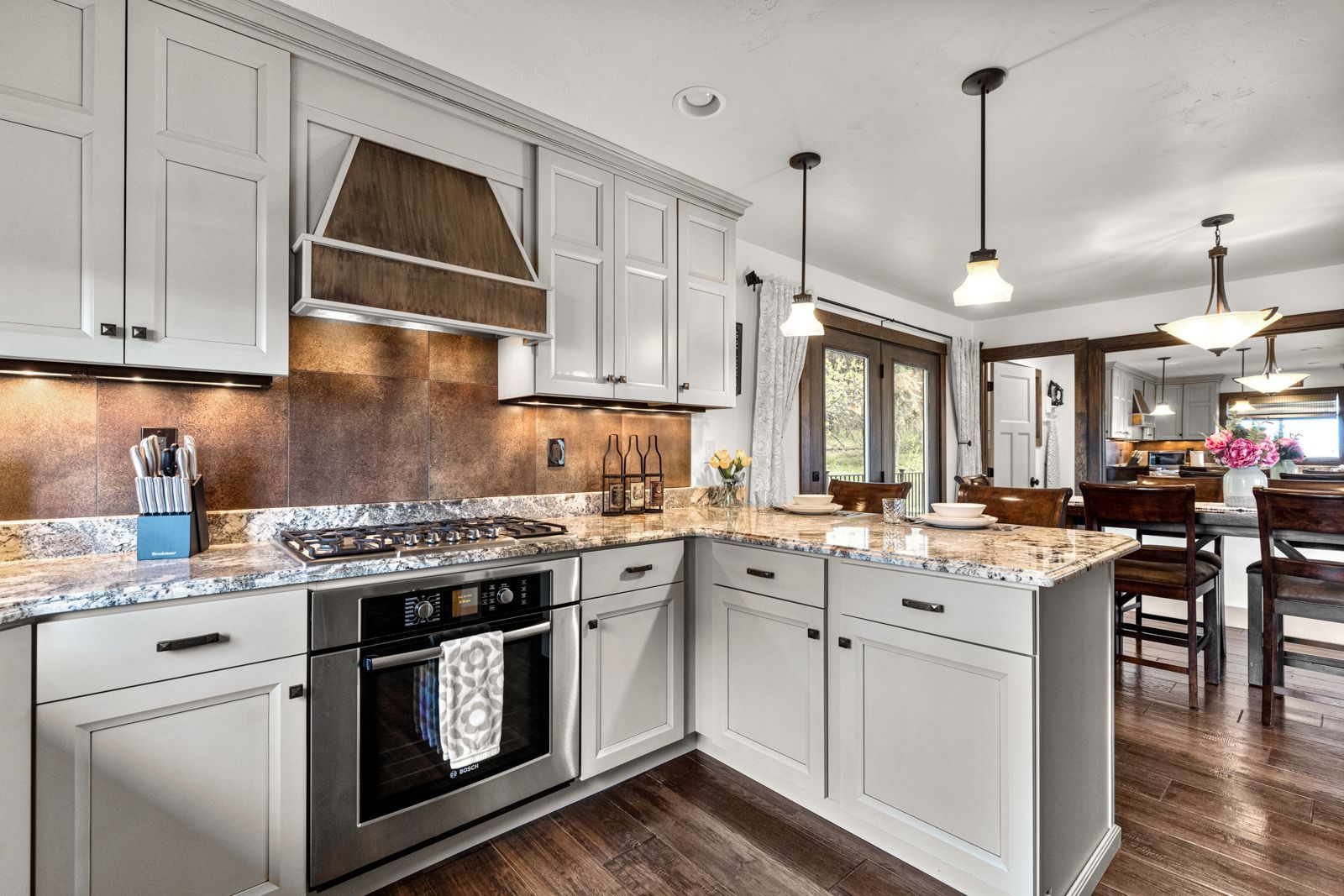 Bright modern kitchen with white cabinets, granite island, stainless appliances, and wood floors