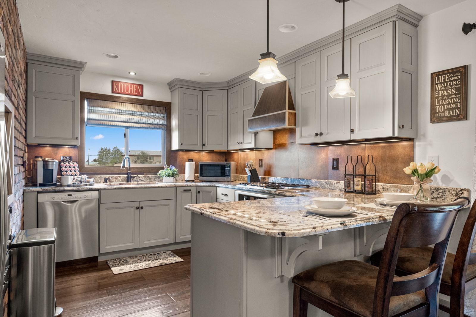 Modern kitchen with gray cabinets, granite island, pendant lights, and a window over the sink