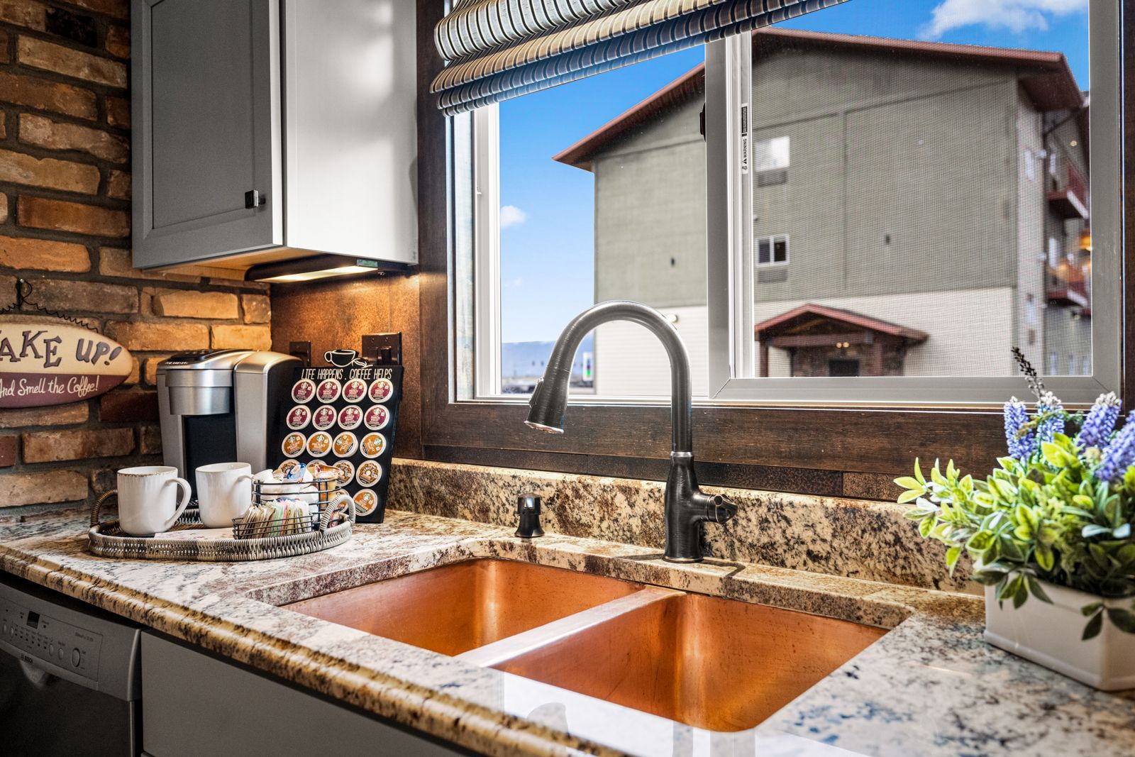 Kitchen sink with granite countertop, coffee mugs, and a window view of houses and blue sky