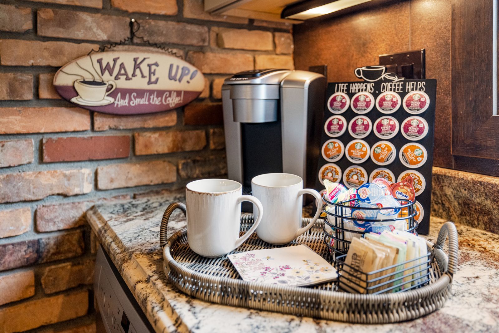 Cozy coffee station with coffee maker, mugs, and K-Cup display on a brick counter.