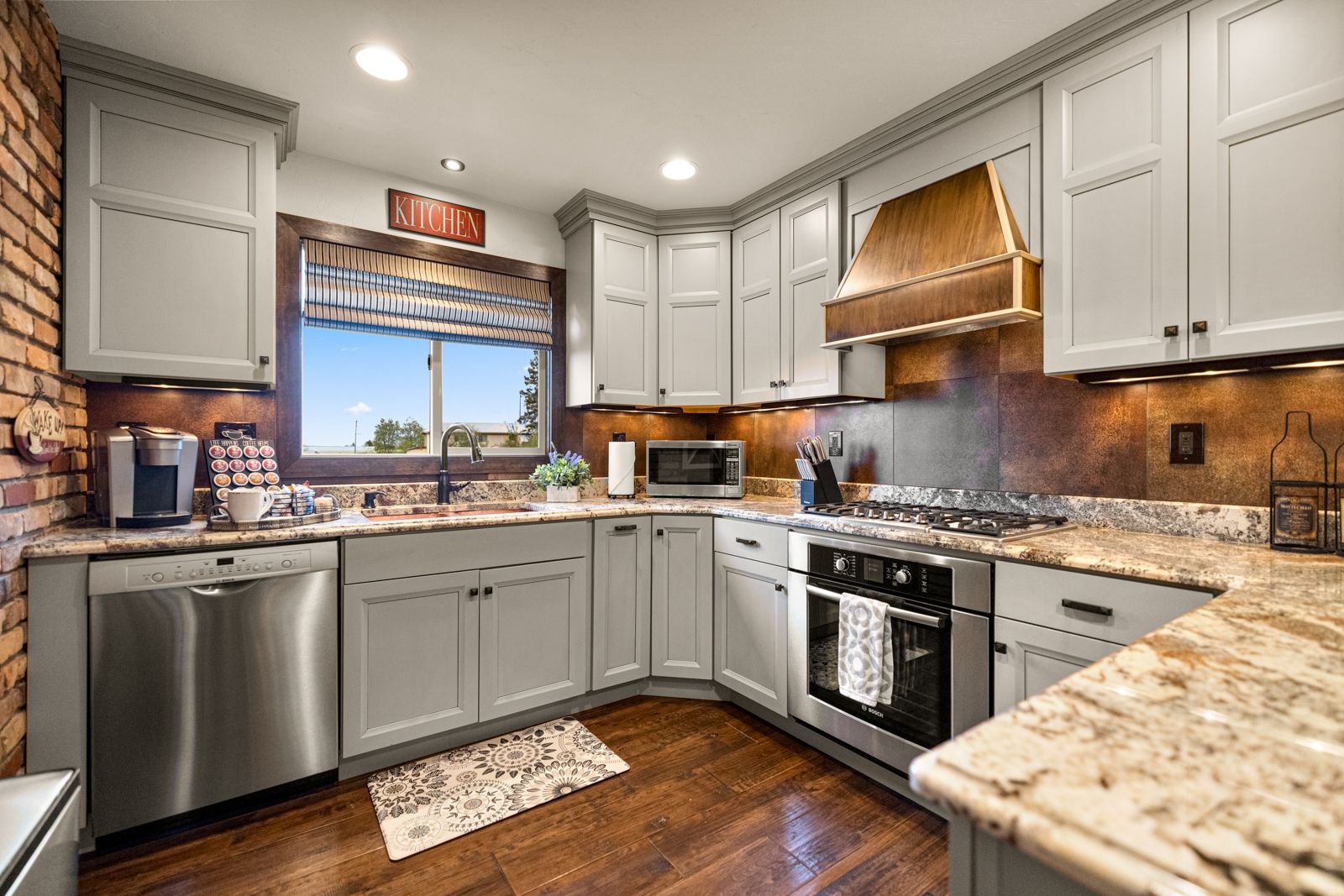 Bright modern kitchen with gray cabinets, stainless appliances, granite counters, and a window over the sink.
