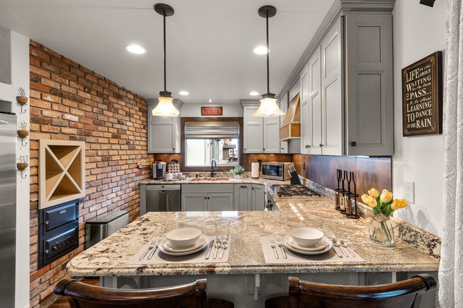 Modern kitchen with granite island, gray cabinets, exposed brick wall, and pendant lights