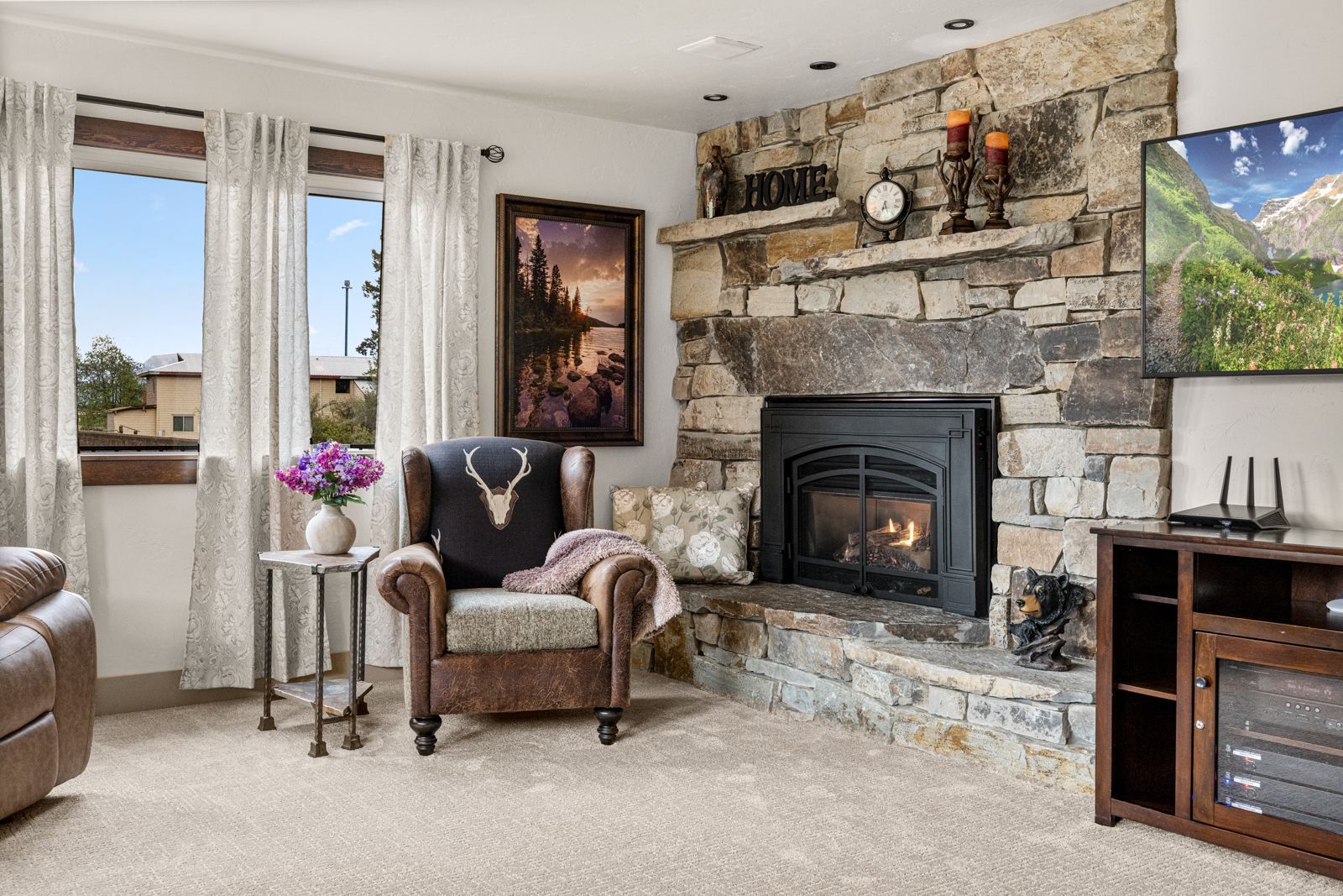 Cozy living room with stone fireplace, armchairs, large windows, and wall art