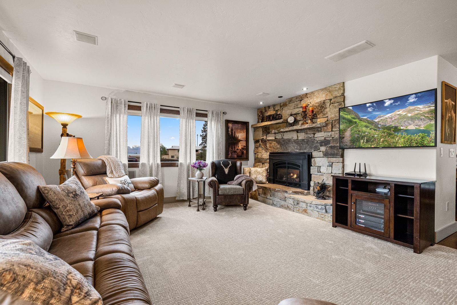 Cozy living room with brown sofa, stone fireplace, large TV, and scenic landscape painting
