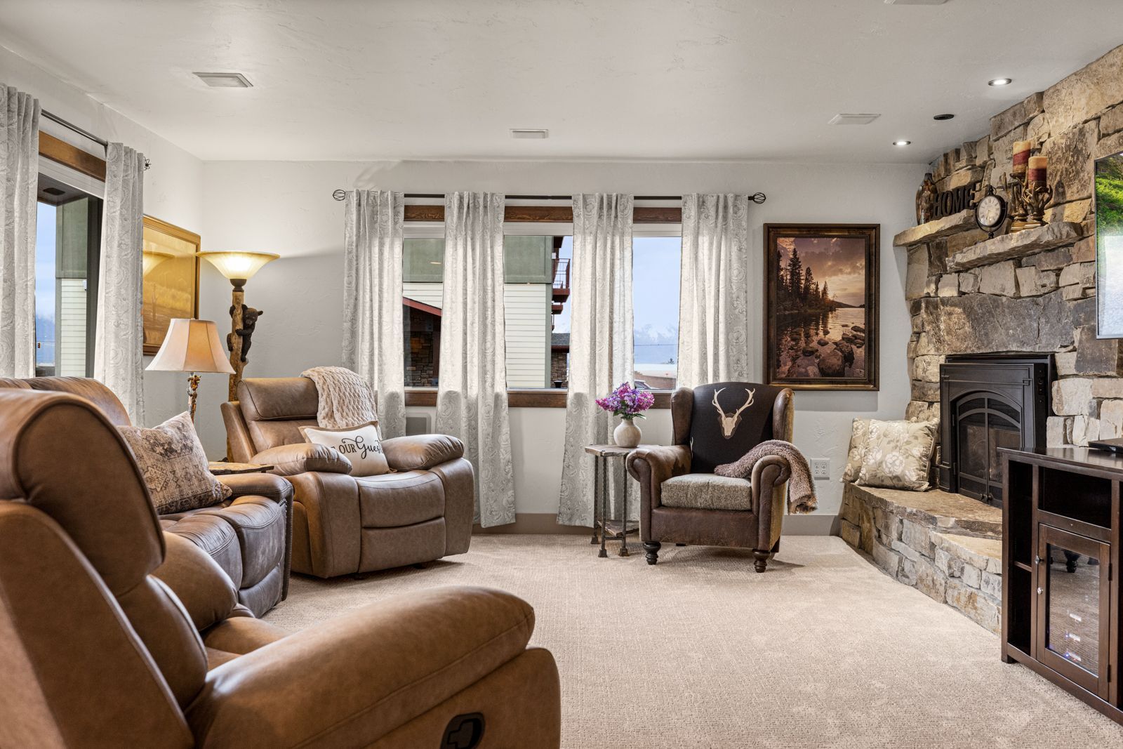 Cozy living room with beige sofas, armchairs, fireplace, and large windows with white curtains.