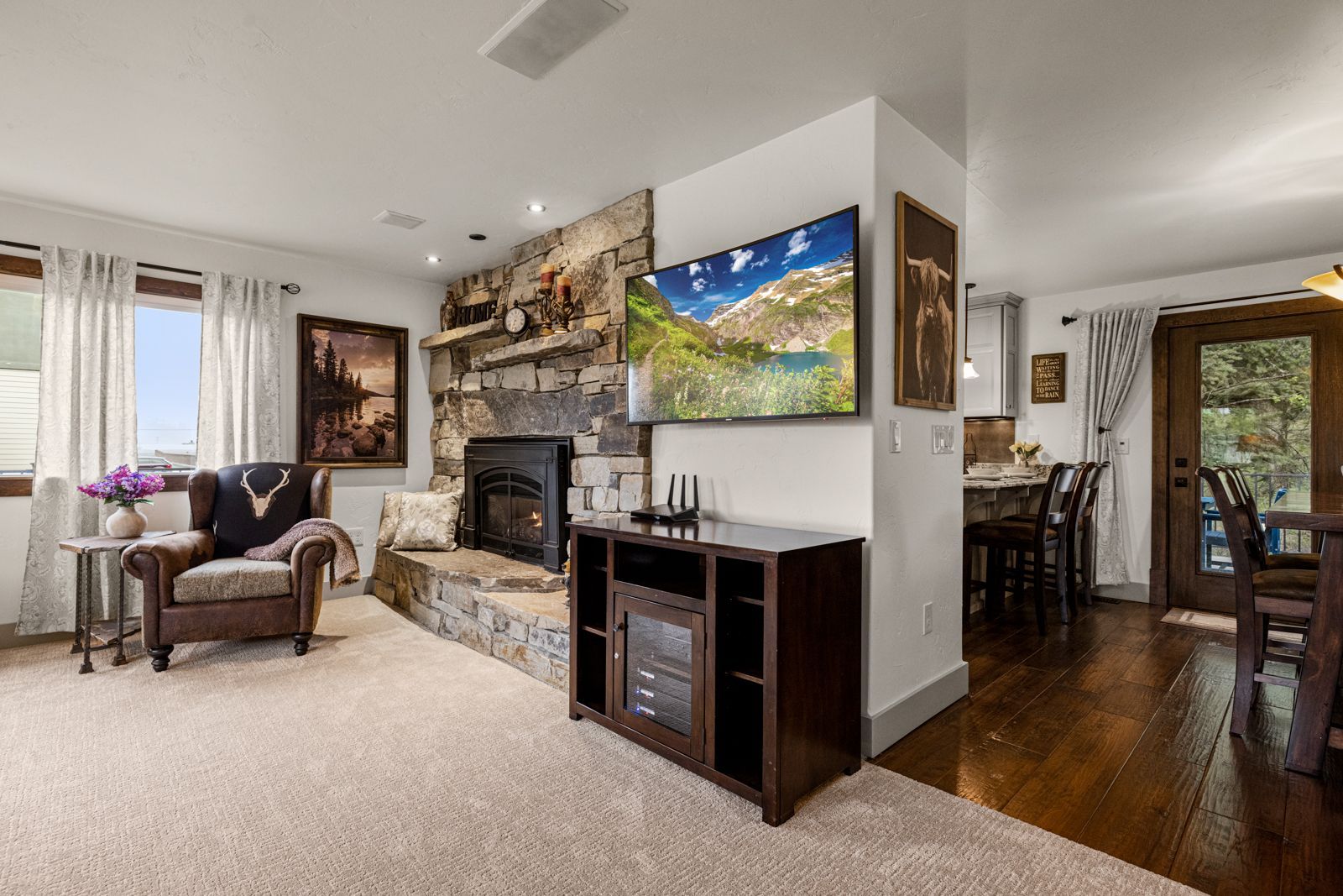 Bright living room with stone fireplace, TV, carpeted seating area, and hardwood dining nook.