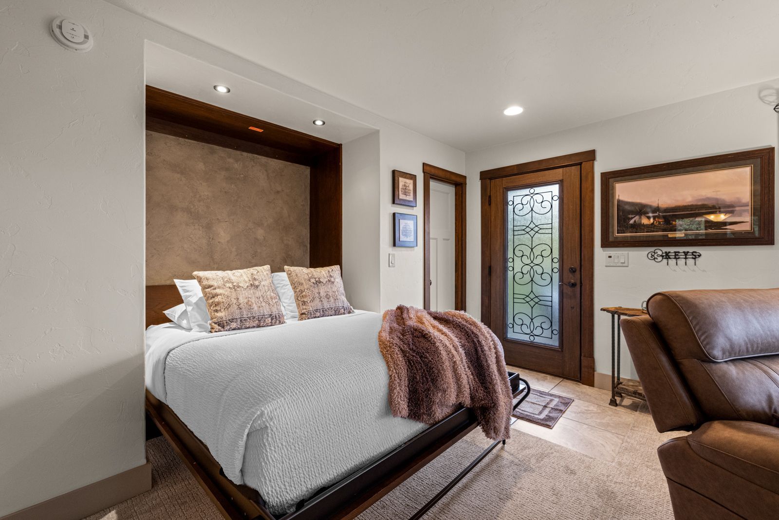 Cozy bedroom with white bedding, wood accents, frosted glass door, and leather chair seating area