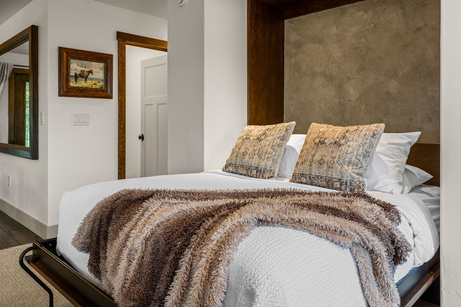 Bedroom with a neatly made bed, textured headboard, and white walls with framed art.