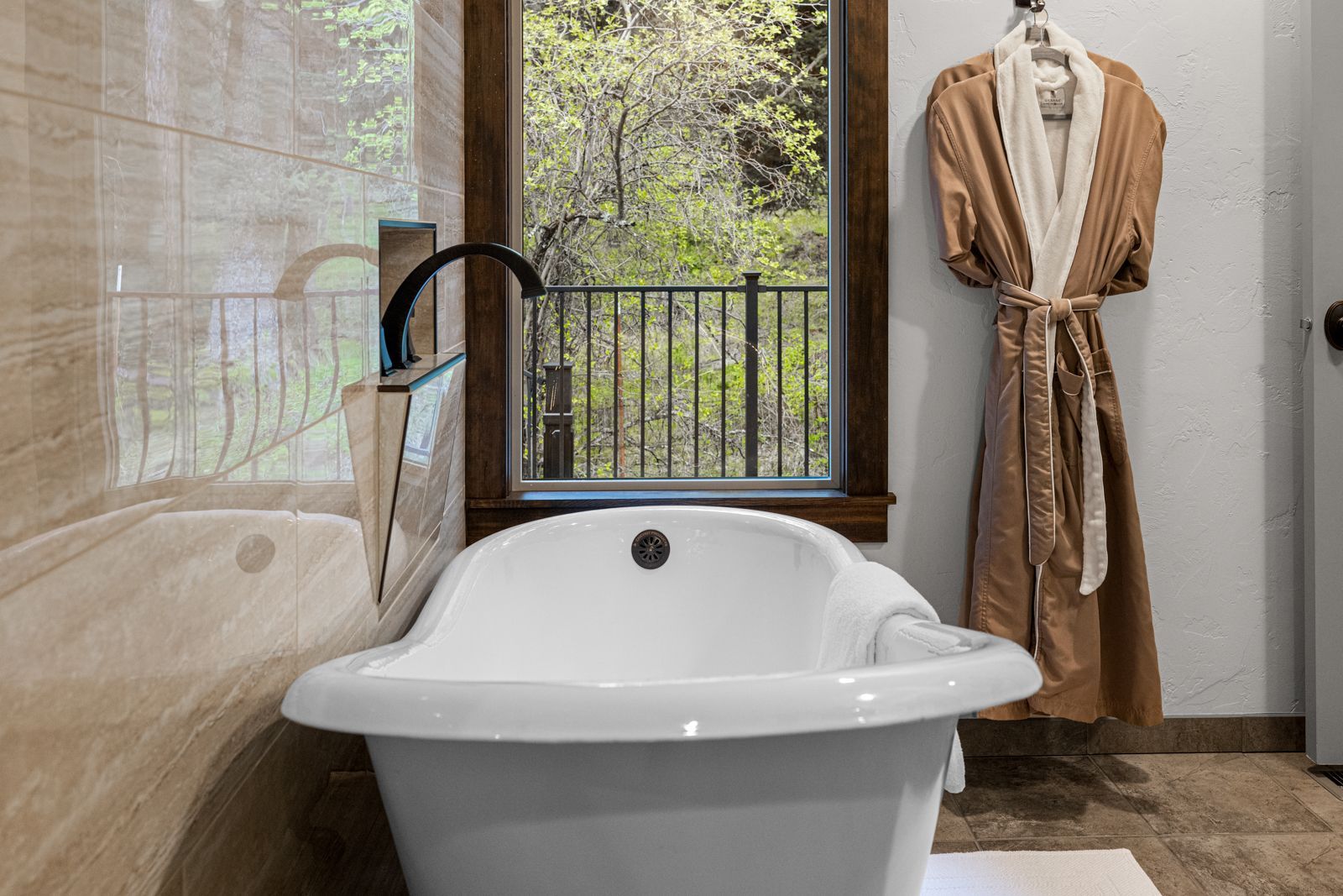 Luxury bathroom with white freestanding tub, black faucet, and robe beside a window overlooking greenery