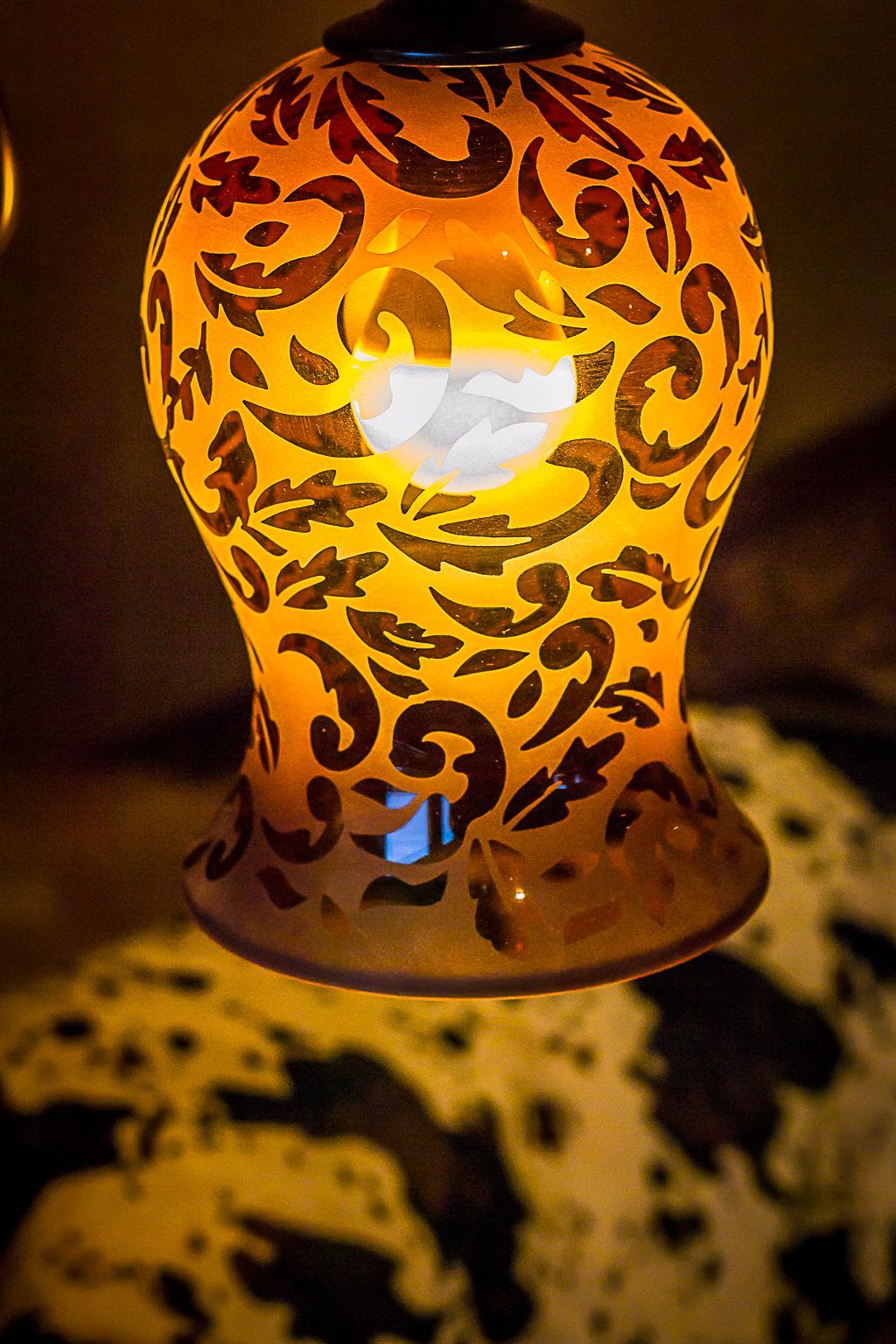 Orange carved glass candle lantern glowing in the dark, casting ornate shadows
