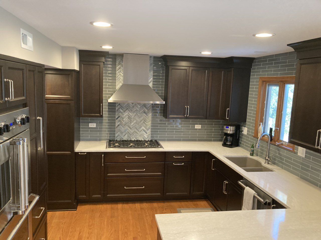 Modern kitchen with dark wood cabinets, stainless range hood, and white countertops under recessed lighting in Arlington Heights, IL
