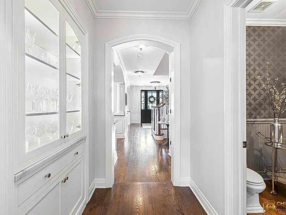 Kitchen remodeling in Glenview, IL, featuring a bright white hallway with wood floors, an arched doorway, and built-in cabinets leading to a room beyond.