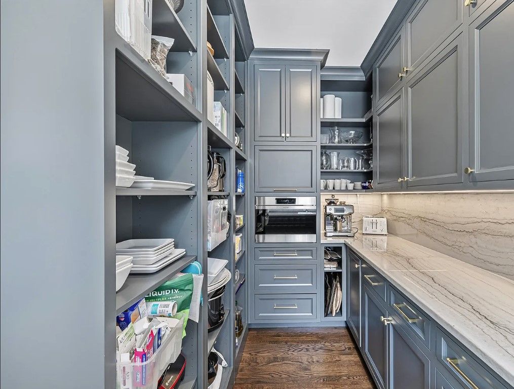 Kitchen remodeling in Glenview, IL, featuring a narrow pantry with gray cabinets, open shelves, wood flooring, and stocked with dishes and supplies.