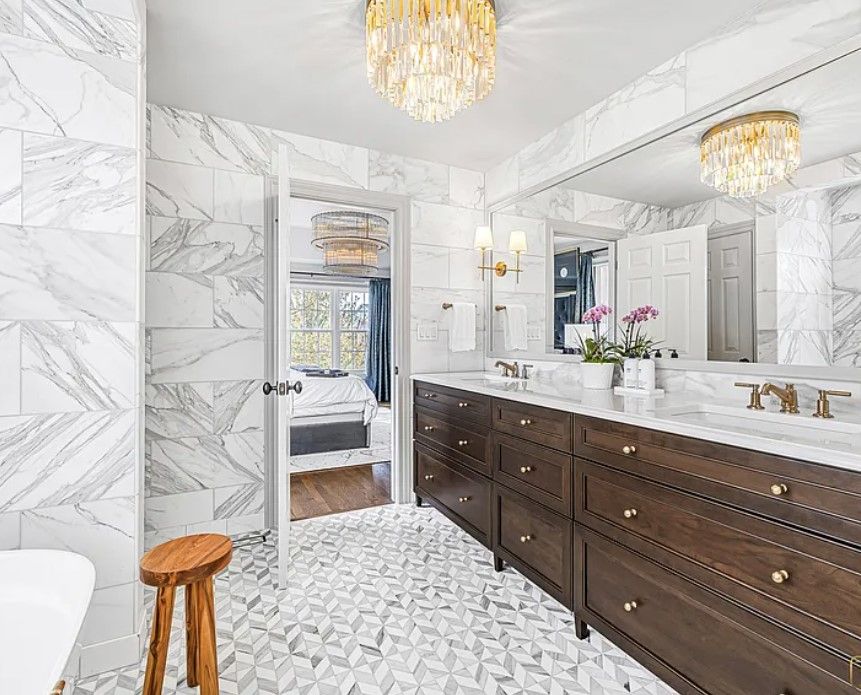 Bright marble bathroom remodeling with dark wood double vanity, large mirror, chandelier, and doorway to a bedroom in Glenview, IL.