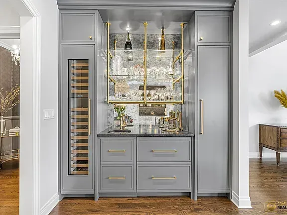 Kitchen remodeling in Glenview, IL, featuring a gray built-in beverage bar with a wine fridge, gold accents, and a mirrored backsplash in a bright hallway.