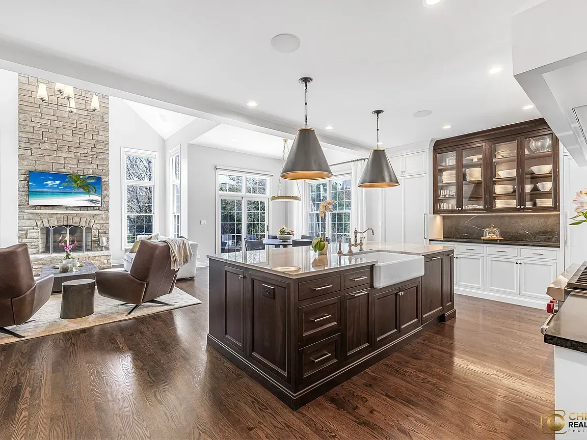Bright modern kitchen remodeling with island, pendant lights, wood floors, and adjoining living area with fireplace in Glenview, IL.