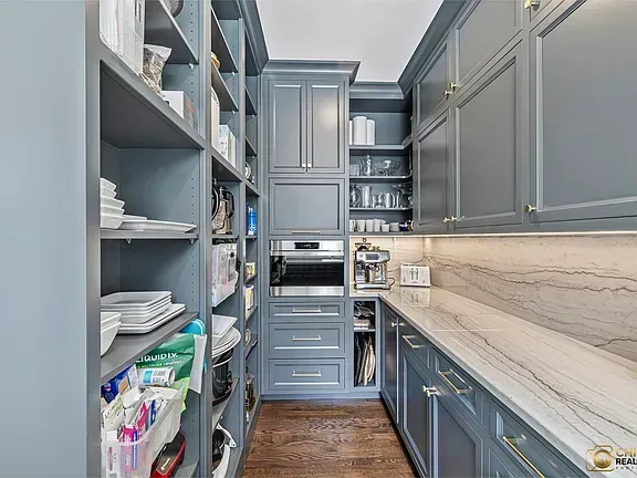 Kitchen remodeling in Glenview, IL, featuring a narrow pantry with gray cabinets, open shelves, white marble backsplash, and wood flooring.