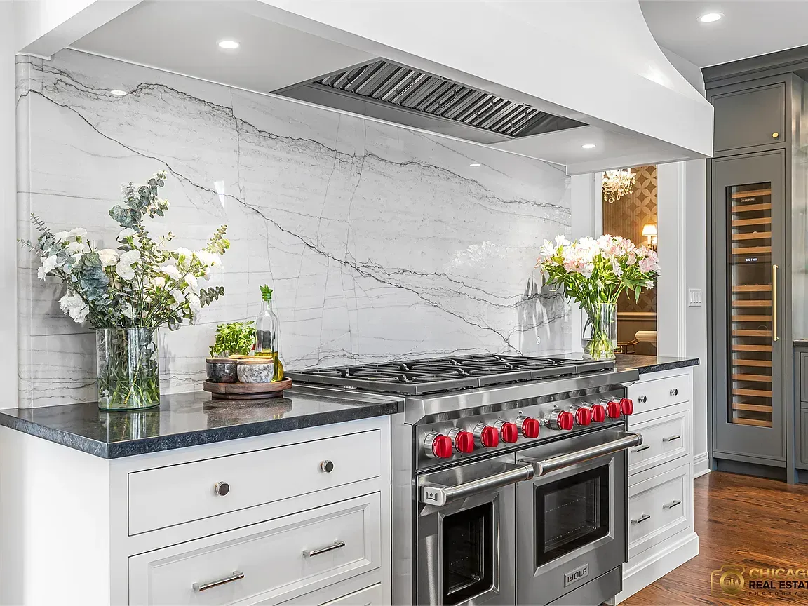 Modern white kitchen remodeling with marble backsplash, black range, and red knobs under a stainless vent hood in Glenview, IL