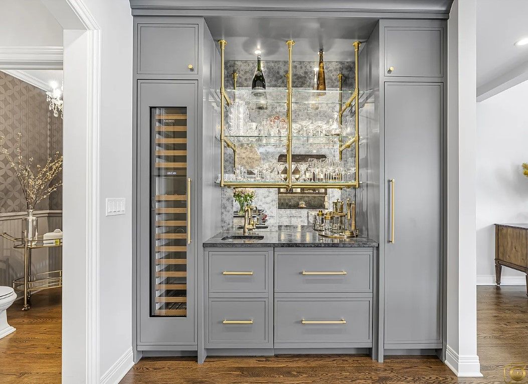 Kitchen remodeling in Glenview, IL, featuring a built-in gray bar cabinet with gold shelves, a mirrored backsplash, and glass doors in a bright room.