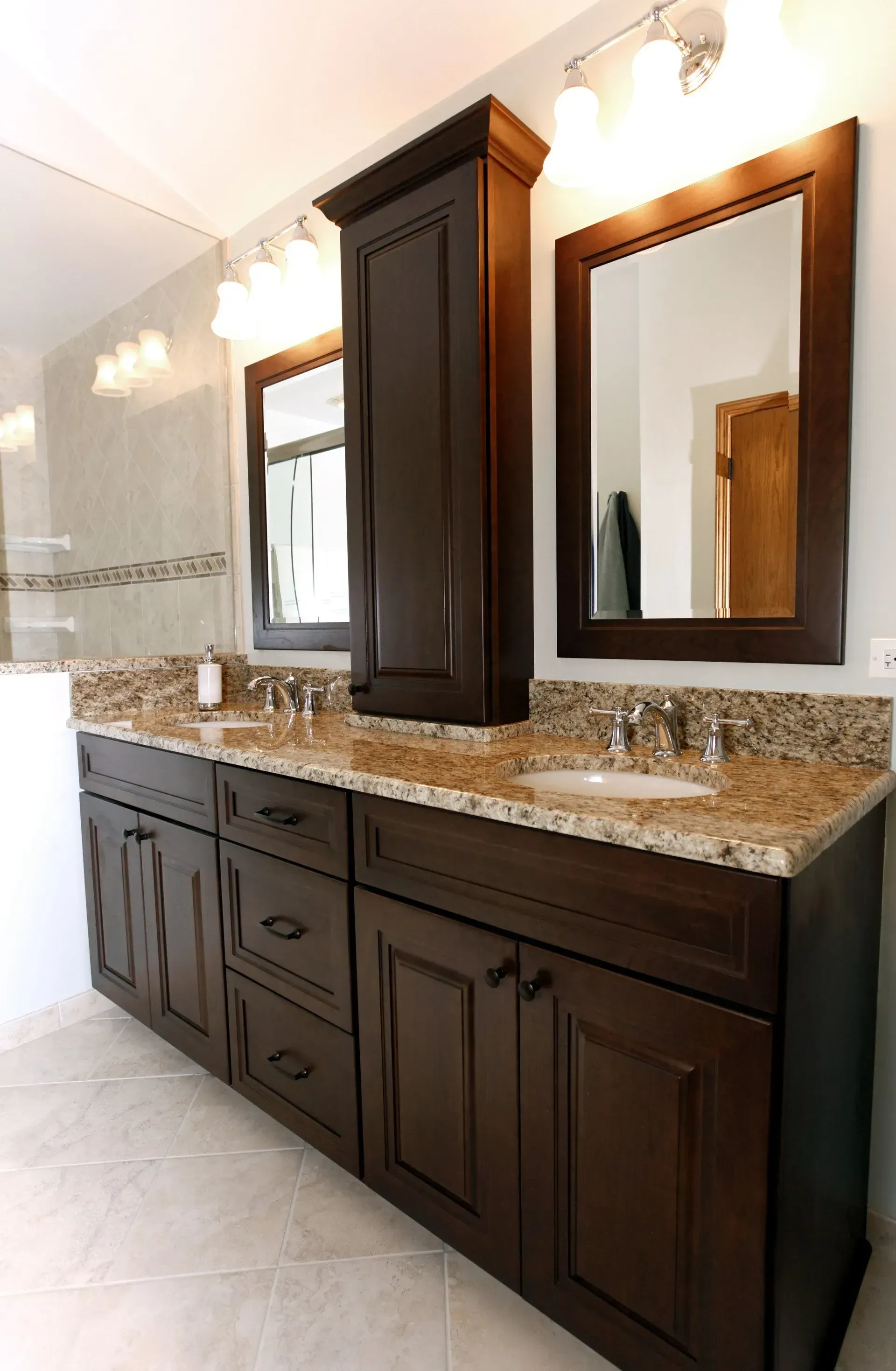 Dark wood double vanity with granite countertop and mirrors in a bright bathroom in a modern kitchen with gray cabinets, island, pendant lights, exposed wood beams, and two barstools in Arlington Heights, IL.