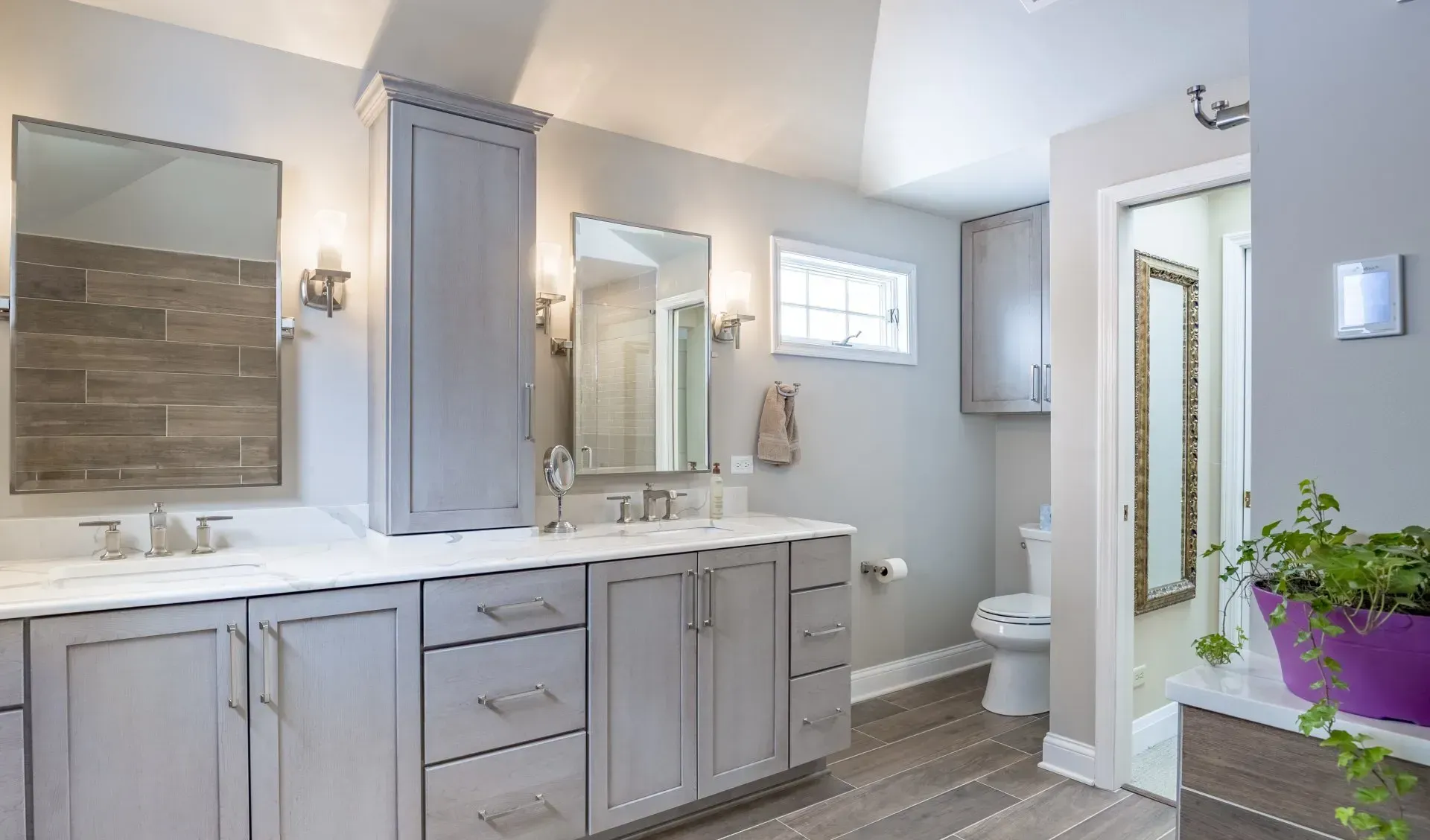 Modern bathroom with double vanity, gray cabinets, large mirrors, and a glass shower door in Modern kitchen with gray cabinets, island, pendant lights, exposed wood beams, and two barstools in Arlington Heights, IL.