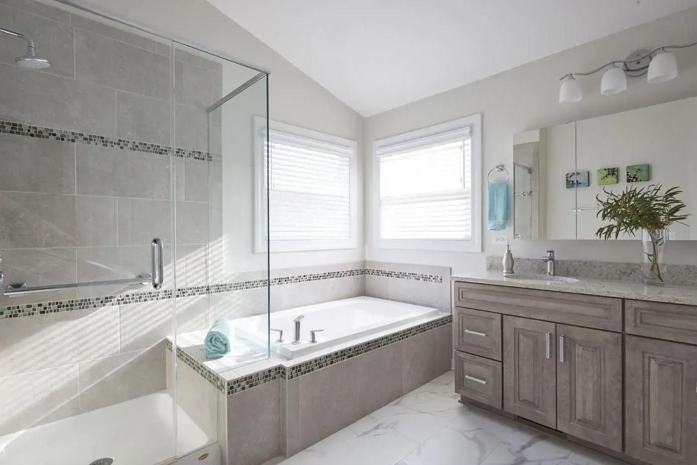 Bright modern bathroom with a glass shower, soaking tub, and gray vanity by a window in Modern kitchen with gray cabinets, island, pendant lights, exposed wood beams, and two barstools in Arlington Heights, IL.