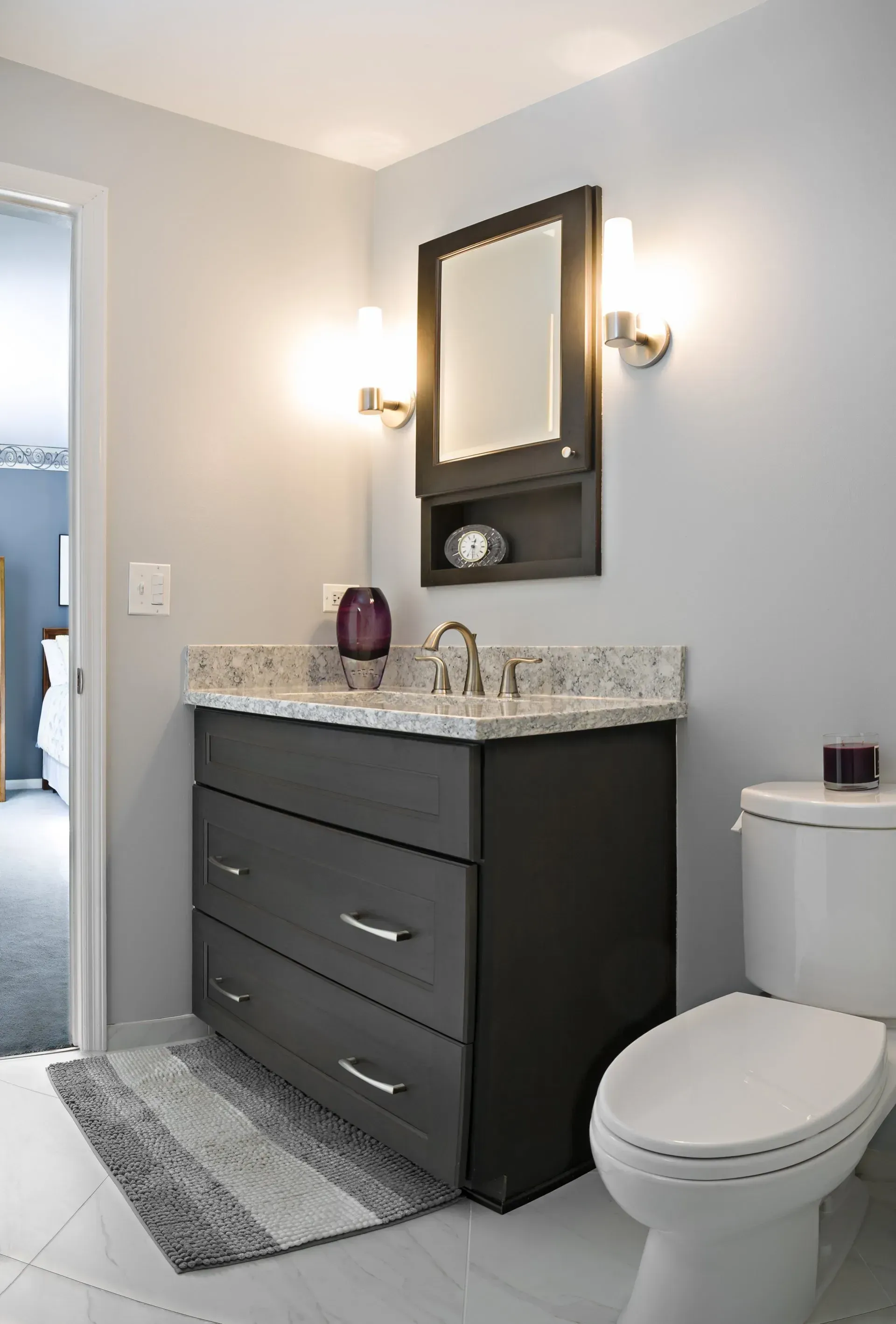 Small modern bathroom with dark vanity, granite countertop, mirror, wall lights, and toilet. In a modern kitchen with gray cabinets, an island, pendant lights, exposed wood beams, and two barstools in Arlington Heights, IL.