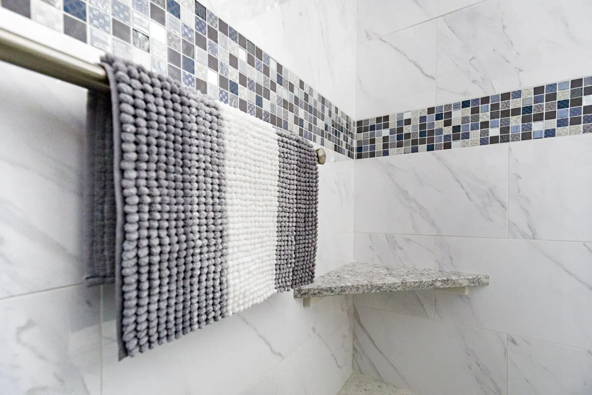 Gray and white bathroom with tiled shower wall and hanging striped towels in Modern kitchen with gray cabinets, island, pendant lights, exposed wood beams, and two barstools in Arlington Heights, IL,