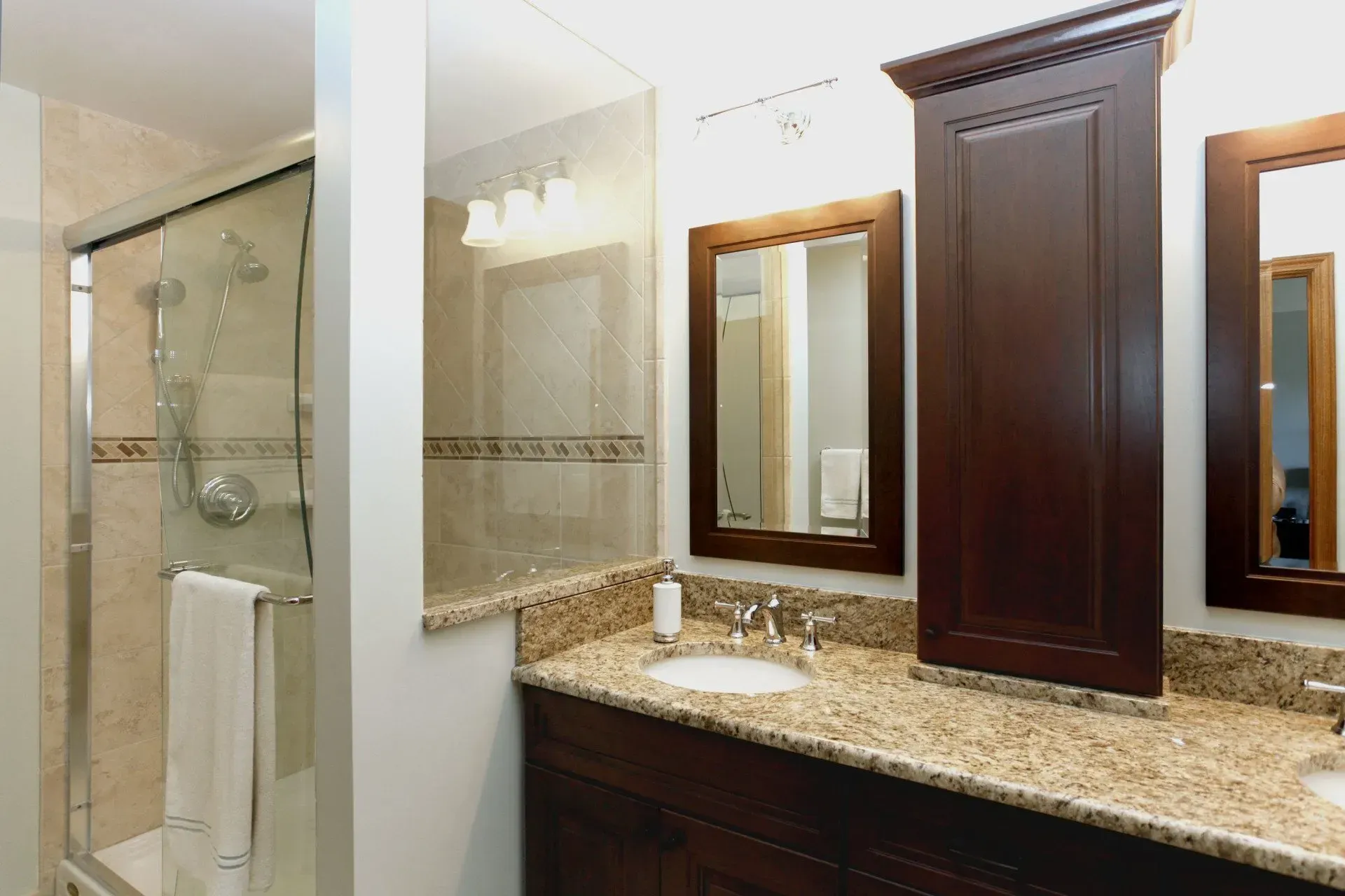 Bathroom with granite vanity, dark wood cabinets, mirror, and glass-enclosed shower. In a modern kitchen with gray cabinets, an island, pendant lights, exposed wood beams, and two barstools in Arlington Heights, IL,