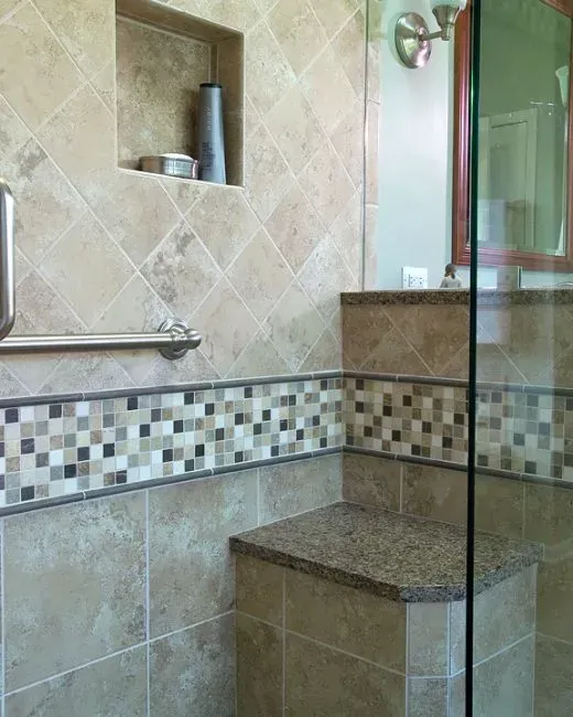 Tiled walk-in shower with glass door, mosaic accent border, and built-in bench in beige stone. In a modern kitchen with gray cabinets, an island, pendant lights, exposed wood beams, and two barstools in Arlington Heights, IL.