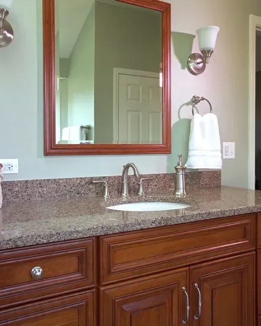 Bathroom vanity with mirror, granite countertop, sink, and towel holder on green wall in Modern kitchen with gray cabinets, island, pendant lights, exposed wood beams, and two barstools in Arlington Heights, IL.