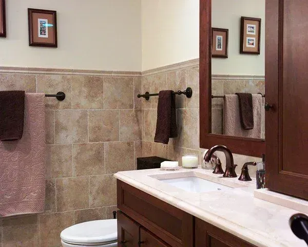 Bathroom vanity with mirror, tan tile walls, brown towels, and a white sink countertop. In a modern kitchen with gray cabinets, an island, pendant lights, exposed wood beams, and two barstools in Arlington Heights, IL.