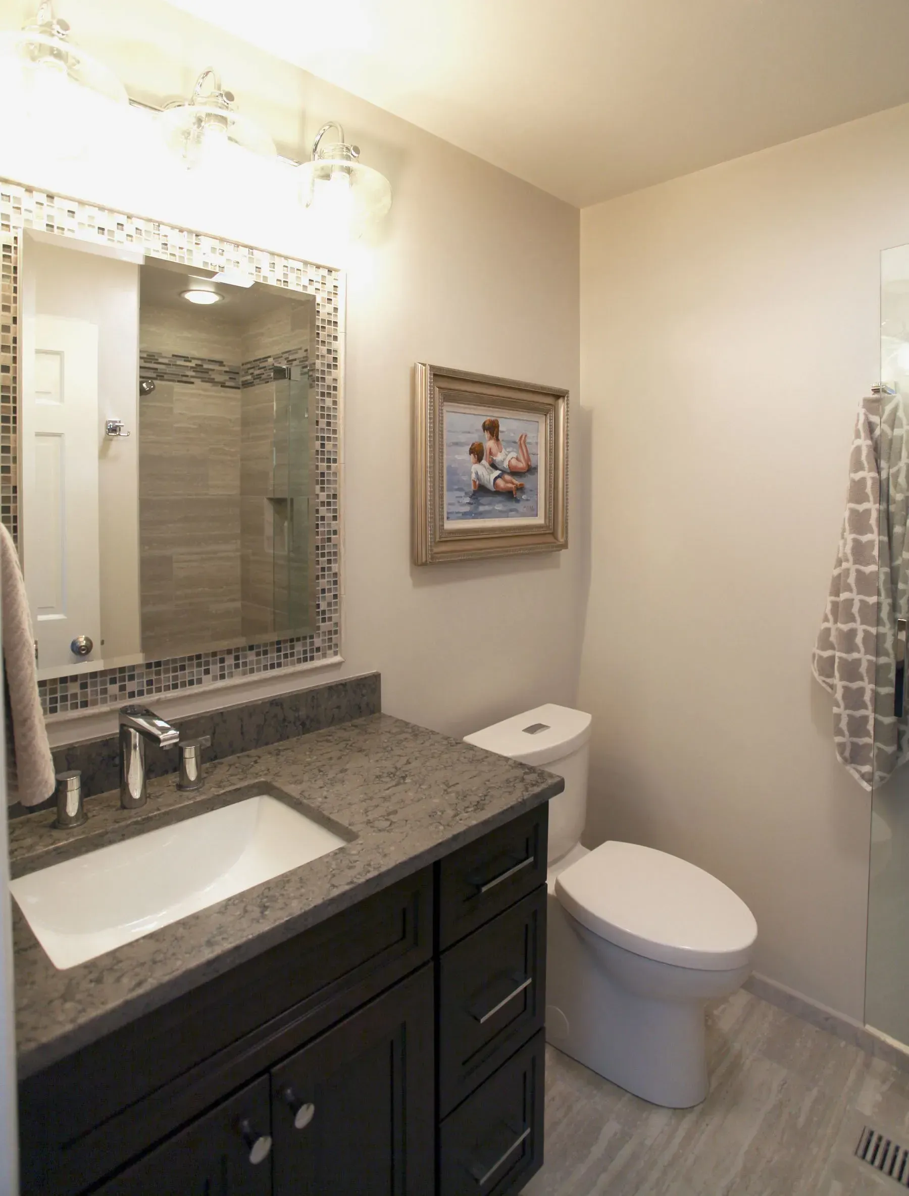 Small bathroom with vanity, sink, mirror, toilet, framed wall art, and gray tiled floor. In a modern kitchen with gray cabinets, an island, pendant lights, exposed wood beams, and two barstools in Arlington Heights, IL, 