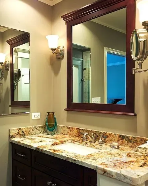 Elegant bathroom vanity with dark wood cabinet, granite countertop, large mirror, and wall sconces in a modern kitchen with gray cabinets, island, pendant lights, exposed wood beams, and two barstools in Arlington Heights, IL. 