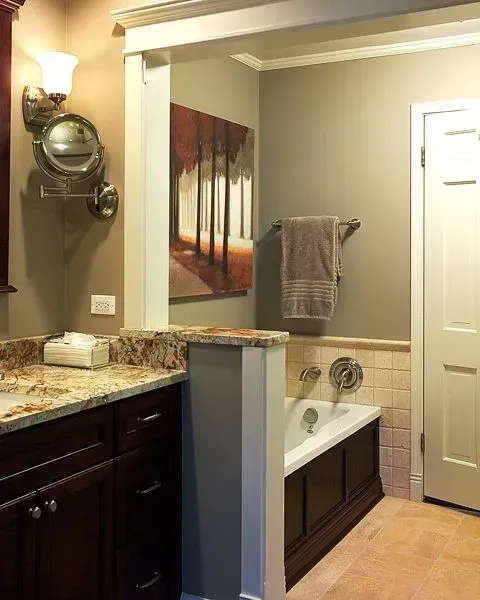 Bathroom with a granite vanity, wall mirror, bathtub, towel rack, and tan tile walls. In a modern kitchen with gray cabinets, an island, pendant lights, exposed wood beams, and two barstools in Arlington Heights, IL.
