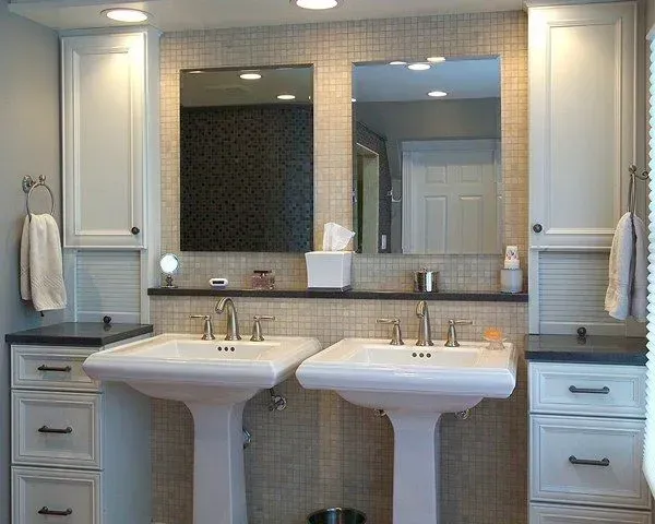 Modern bathroom with two pedestal sinks, double mirrors, and built-in cabinets around a central vanity. In a modern kitchen with gray cabinets, an island, pendant lights, exposed wood beams, and two barstools in Arlington Heights, IL.
