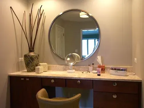 Bathroom vanity with round mirror, dark wood cabinets, beige walls, and decorative vase on the counter in a Modern kitchen with gray cabinets, island, pendant lights, exposed wood beams, and two barstools in Arlington Heights, IL.