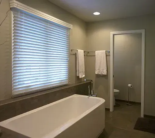 Modern bathroom with a freestanding tub, window blinds, towel bars, and walk-in shower attachment in Modern kitchen with gray cabinets, island, pendant lights, exposed wood beams, and two barstools in Arlington Heights, IL.