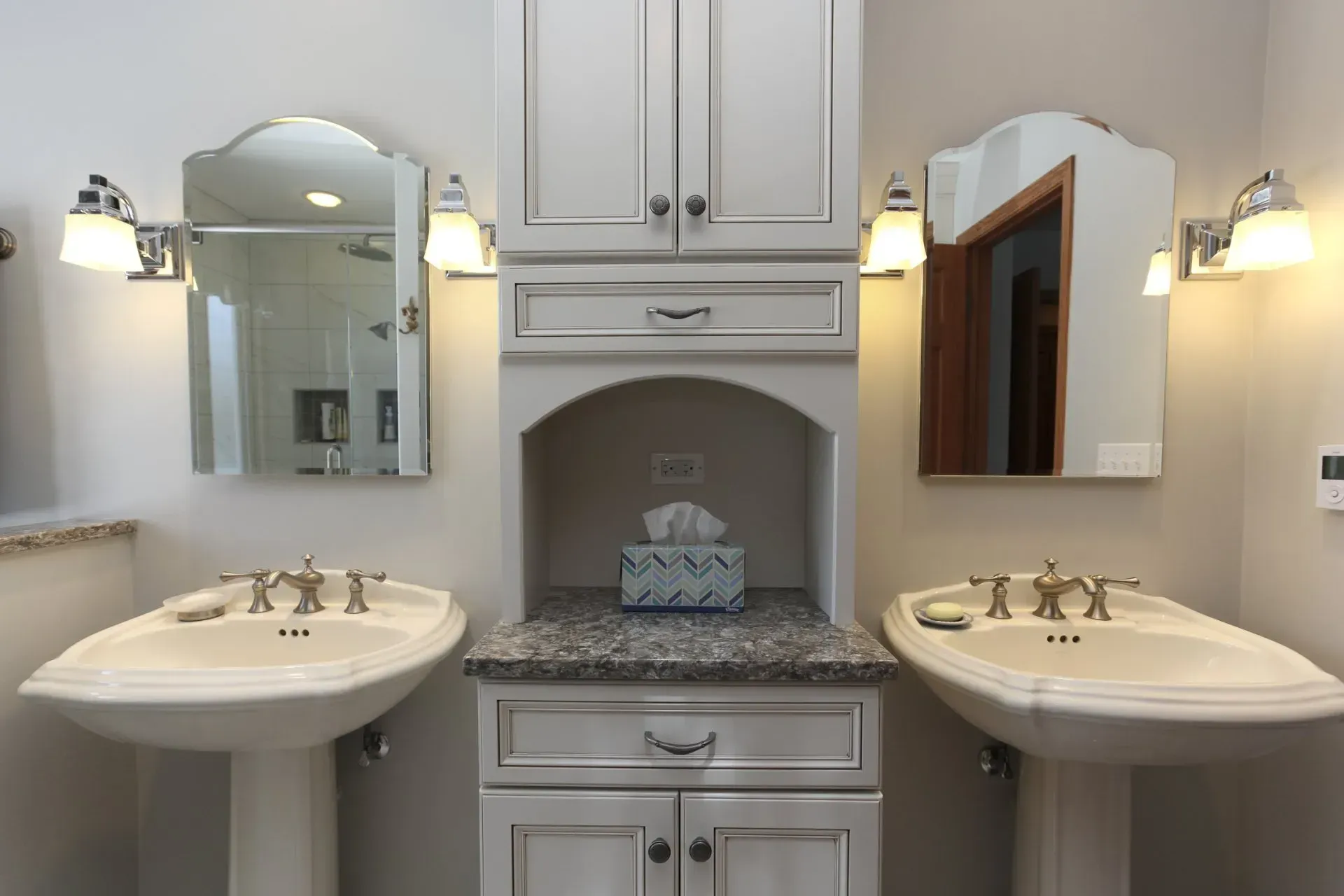 Elegant bathroom with two pedestal sinks, mirrors, sconces, and a central cabinet with a granite countertop. In a modern kitchen with gray cabinets, an island, pendant lights, exposed wood beams, and two barstools in Arlington Heights, IL.