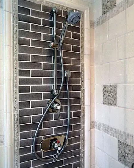 Shower with chrome fixture and handheld sprayer against dark brick and beige tile walls in a modern kitchen with gray cabinets, island, pendant lights, exposed wood beams, and two barstools in Arlington Heights, IL.