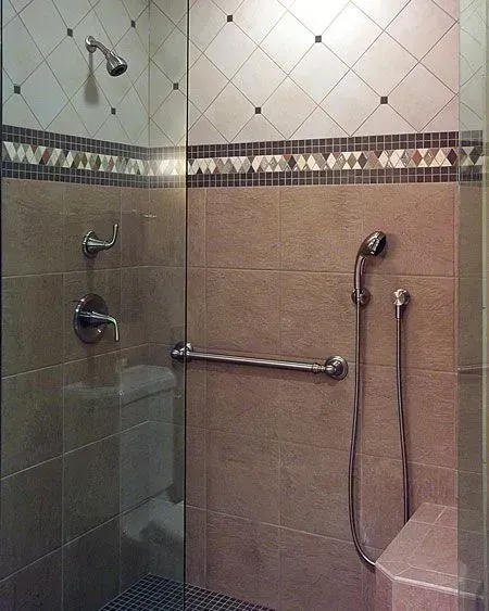 Accessible shower stall with grab bars, handheld showerhead, and tiled walls in a modern kitchen with gray cabinets, island, pendant lights, exposed wood beams, and two barstools in Arlington Heights, IL.