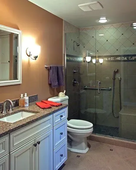 Bathroom with vanity, toilet, and glass-enclosed shower in beige and white tones. in a modern kitchen with gray cabinets, an island, pendant lights, exposed wood beams, and two barstools in Arlington Heights, IL.