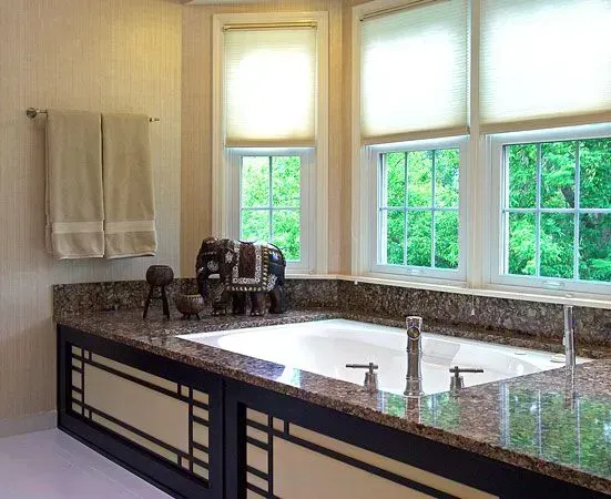 Bright bathroom with granite double sink vanity, towel, decorative elephant, and large sunlit windows overlooking greenery in Modern kitchen with gray cabinets, island, pendant lights, exposed wood beams, and two barstools in Arlington Heights, IL.