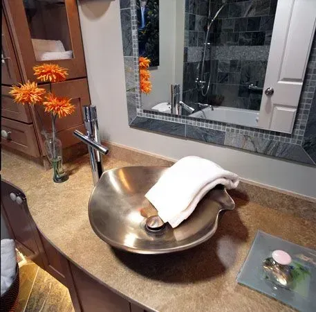 Bathroom remodeling in Arlington Heights, IL, featuring a vanity with a copper vessel sink, chrome faucet, white towel, and orange flowers by the mirror.