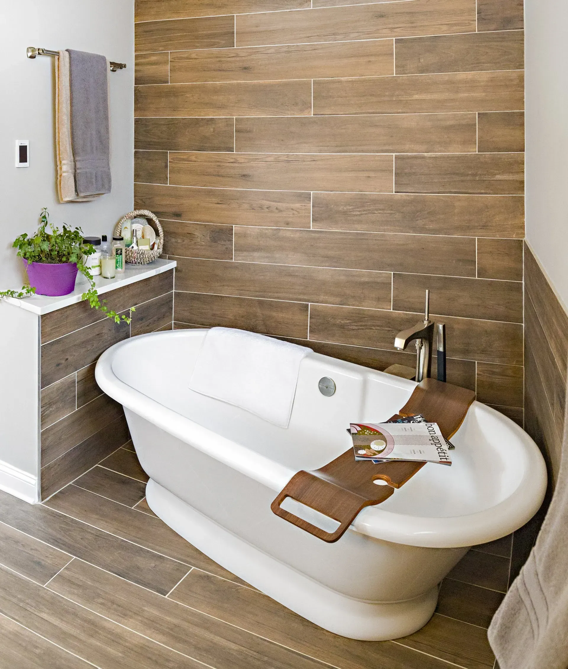 Modern bathroom with a white freestanding tub, wood tile walls and floor, and a small side table. In Lake Zurich, IL.