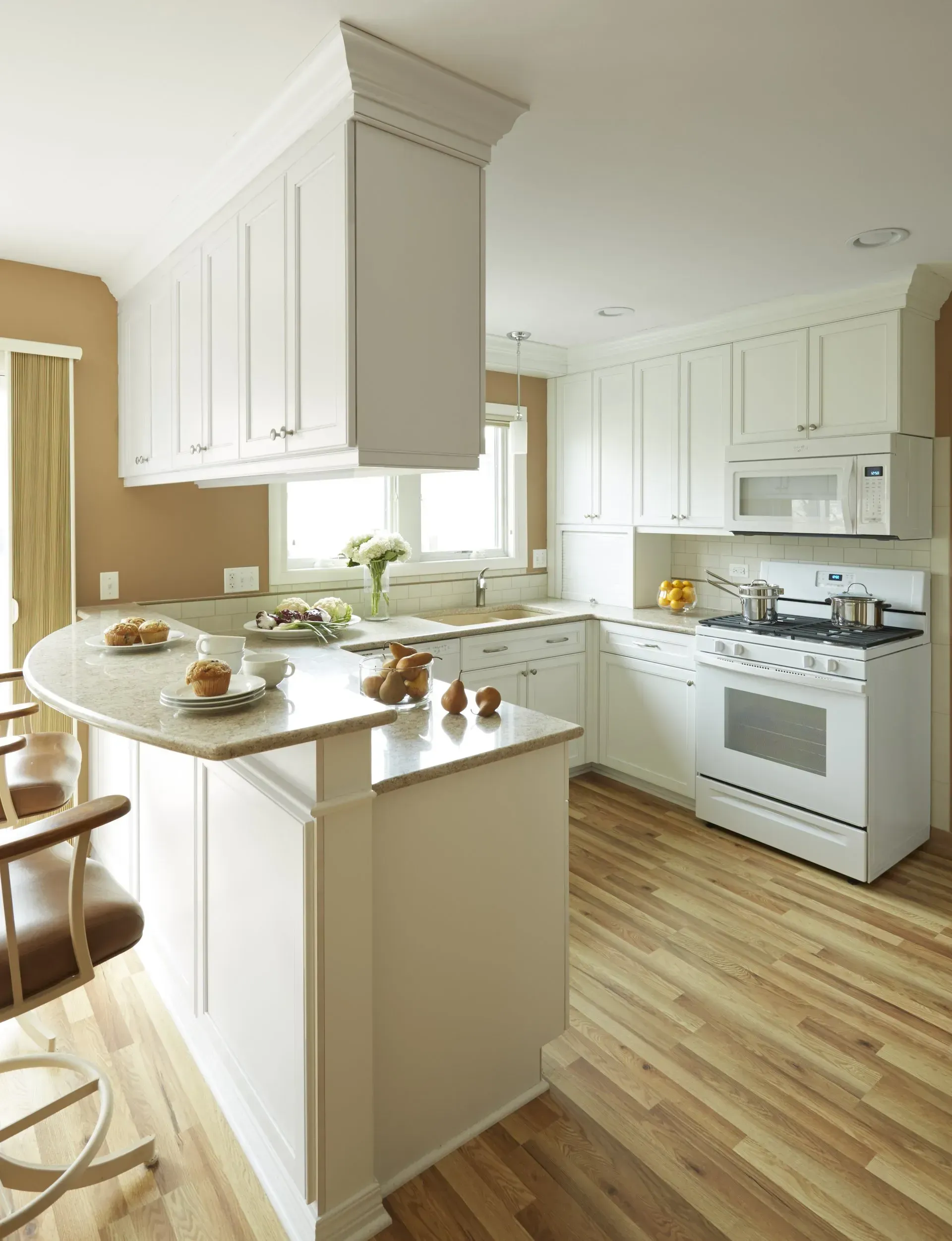 Bright white kitchen remodeling with island, hardwood floors, and stove by a window in Arlington Heights, IL.